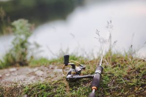 Photo moulinet de canne à pêche sur herbe fond rivière - Activités en montagne