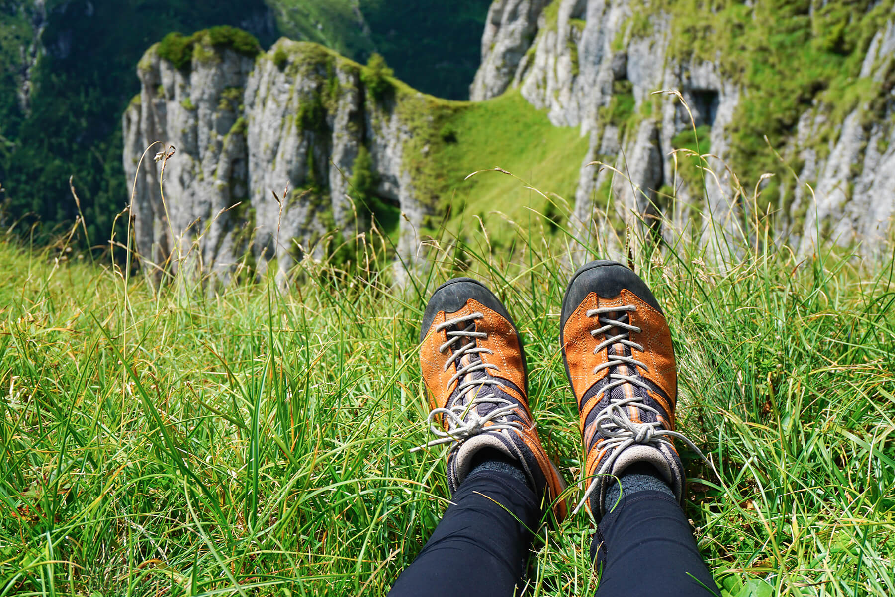 Photo chaussures de randonnée orange pour femme contre sol herbeux et montagnes